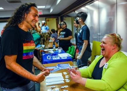 A student wearing an L G B T pride shirt talks to a volunteer running a table at an event.